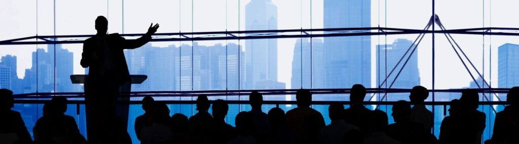 Someone speaking to an audience with a city skyline as a backdrop