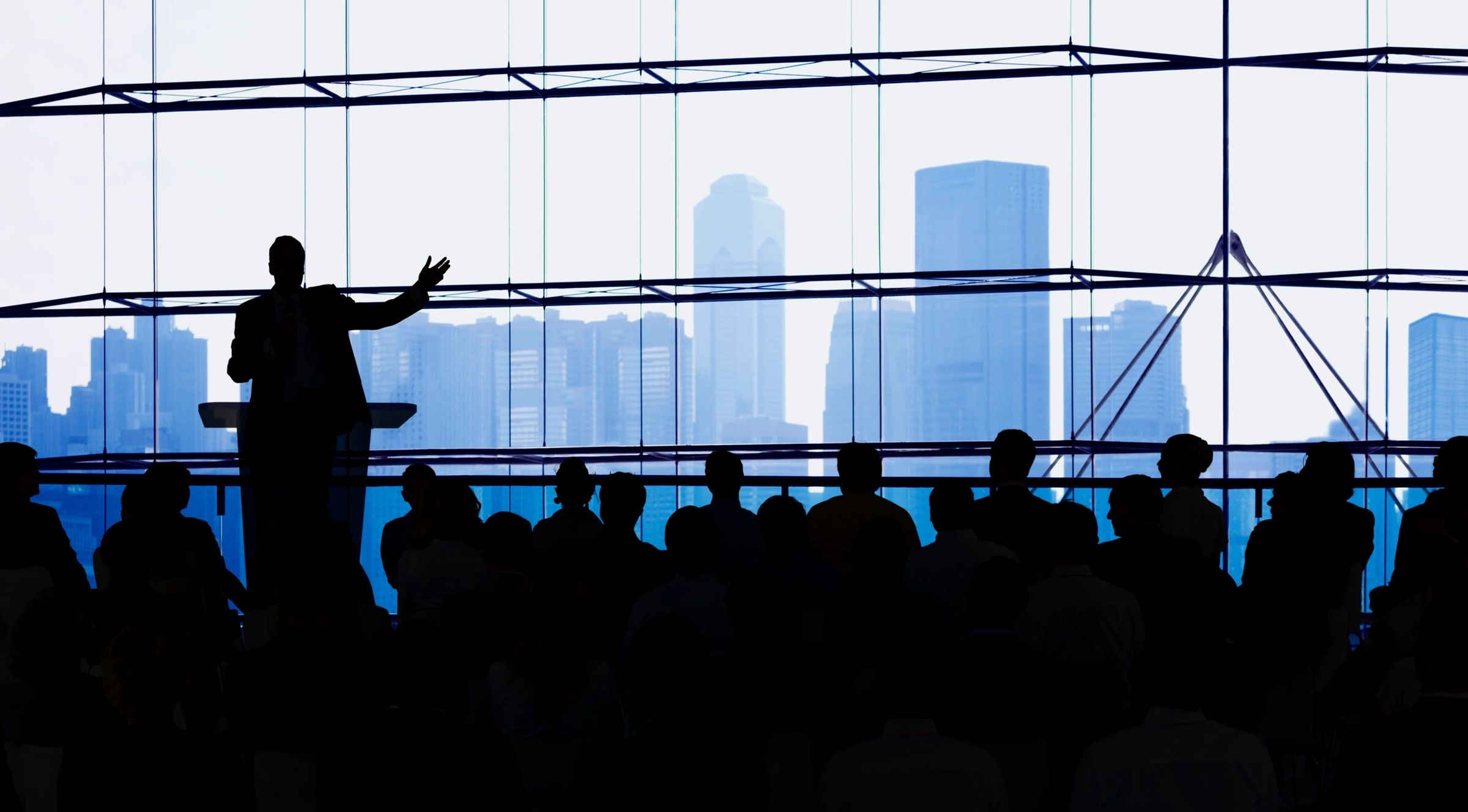 Someone speaking to an audience with a city skyline as a backdrop